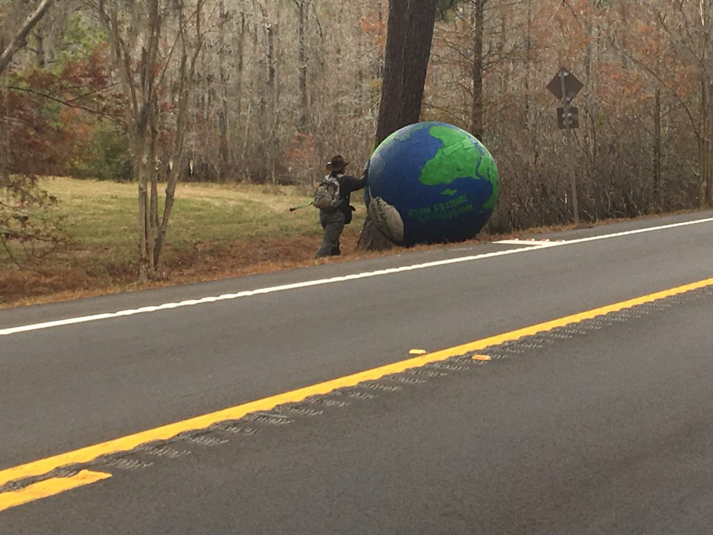 A man rolling a globe along US 90.